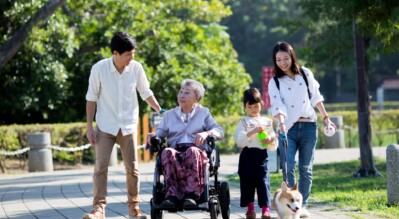 An-elder-in-a-travel-power-wheelchair-going-around-the-park-with-her-family