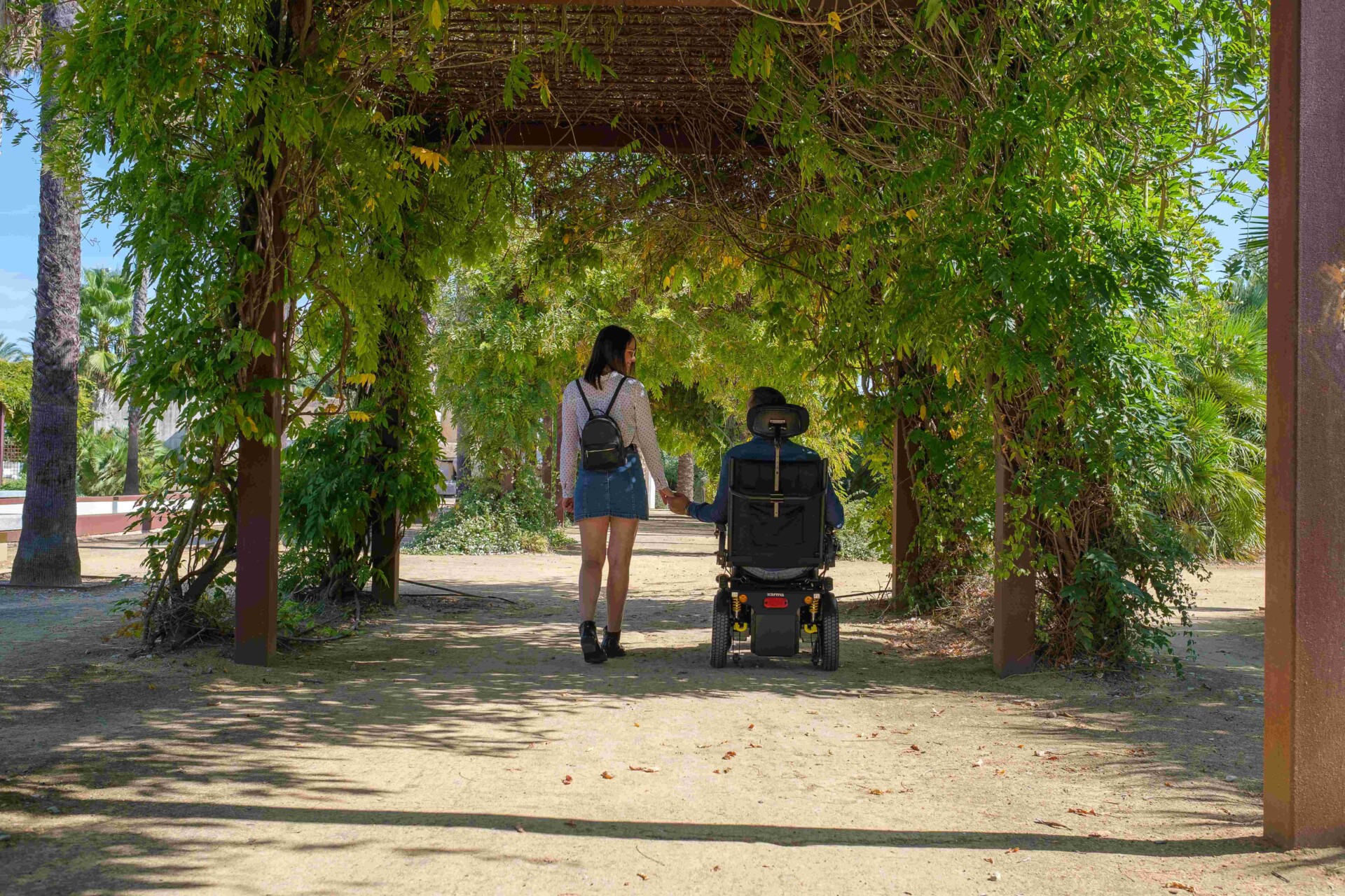  A-man-in-a-power-wheelchair-holding-his-hand-with-a-woman-in-a-park