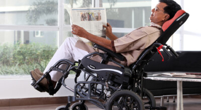 A man reading comfortably in a tilt-in-space wheelchair.
