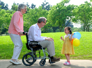 An-elder-in-travel-wheelchair-with-an-elderly-female-caregiver-talking-with-a-little-girl-in-a-park