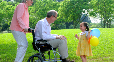 An-elder-in-travel-wheelchair-with-an-elderly-female-caregiver-talking-with-a-little-girl-in-a-park