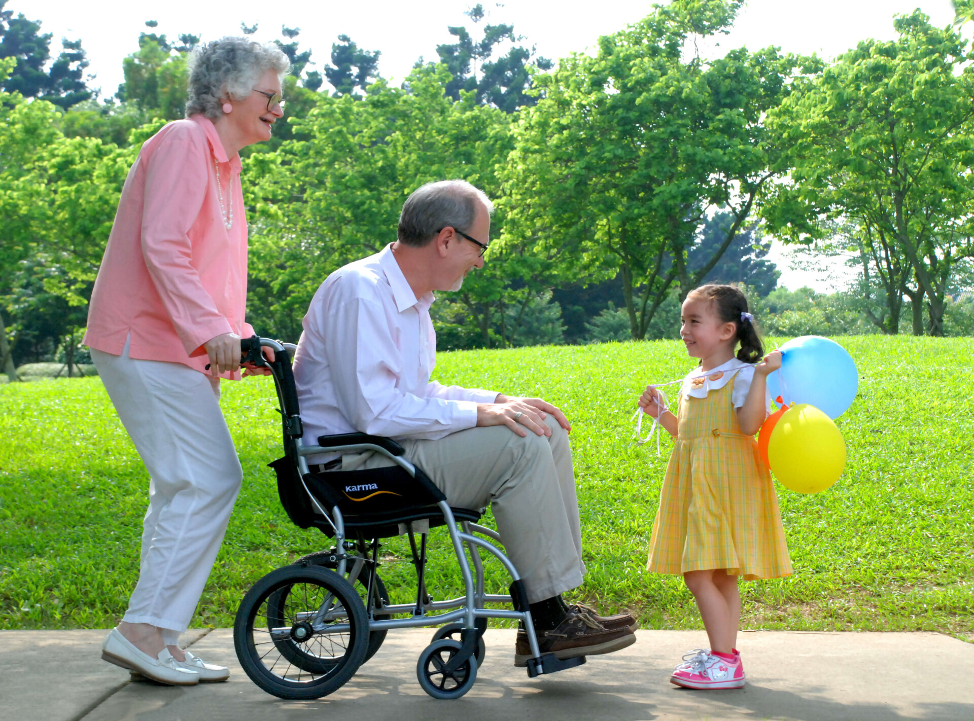 An-elder-in-travel-wheelchair-with-an-elderly-female-caregiver-talking-with-a-little-girl-in-a-park