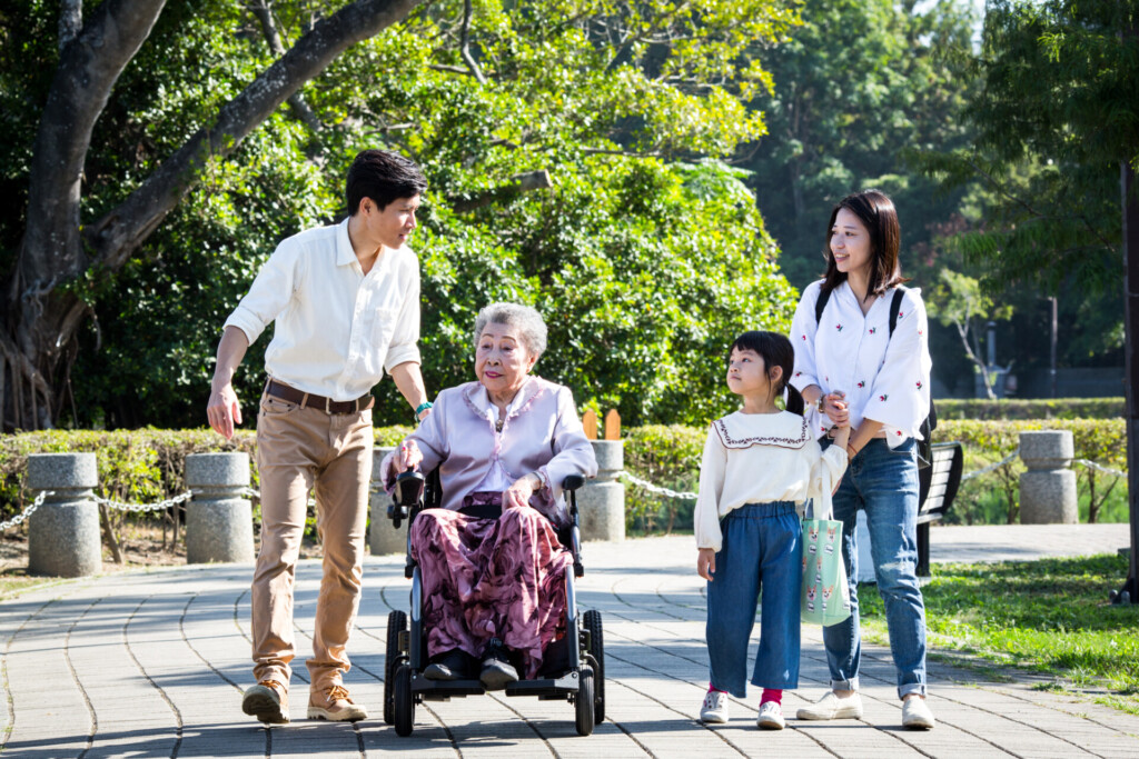 An-elder-in-a-travel-power-wheelchair-going-around-the-park-with-her-family 