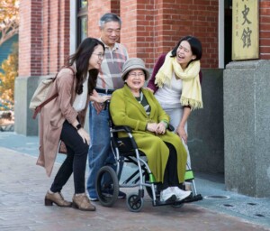 An-elder-lady-in-a-wheelchair-surrounded-by-her-family-in-the-front-of-a-building