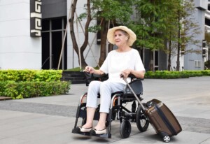 An-elderly-woman-traveller-in-a-power-wheelchair-carrying-her-suitcase-on-the-street