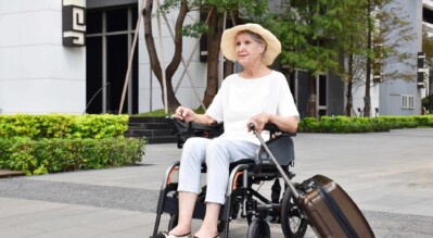 An-elderly-woman-traveller-in-a-power-wheelchair-carrying-her-suitcase-on-the-street